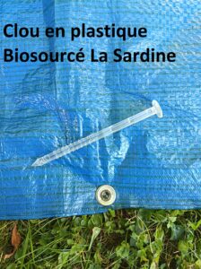 Photo montrant un clou en plastique bio sourcé transparent, fixant une bâche au sol. Fabriqué par la société SEI Sarl