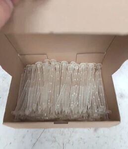 Photo montrant un clou en plastique bio sourcé transparent, dans leur carton de conditionnement par 100 pièces. Fabriqué par la société SEI Sarl
